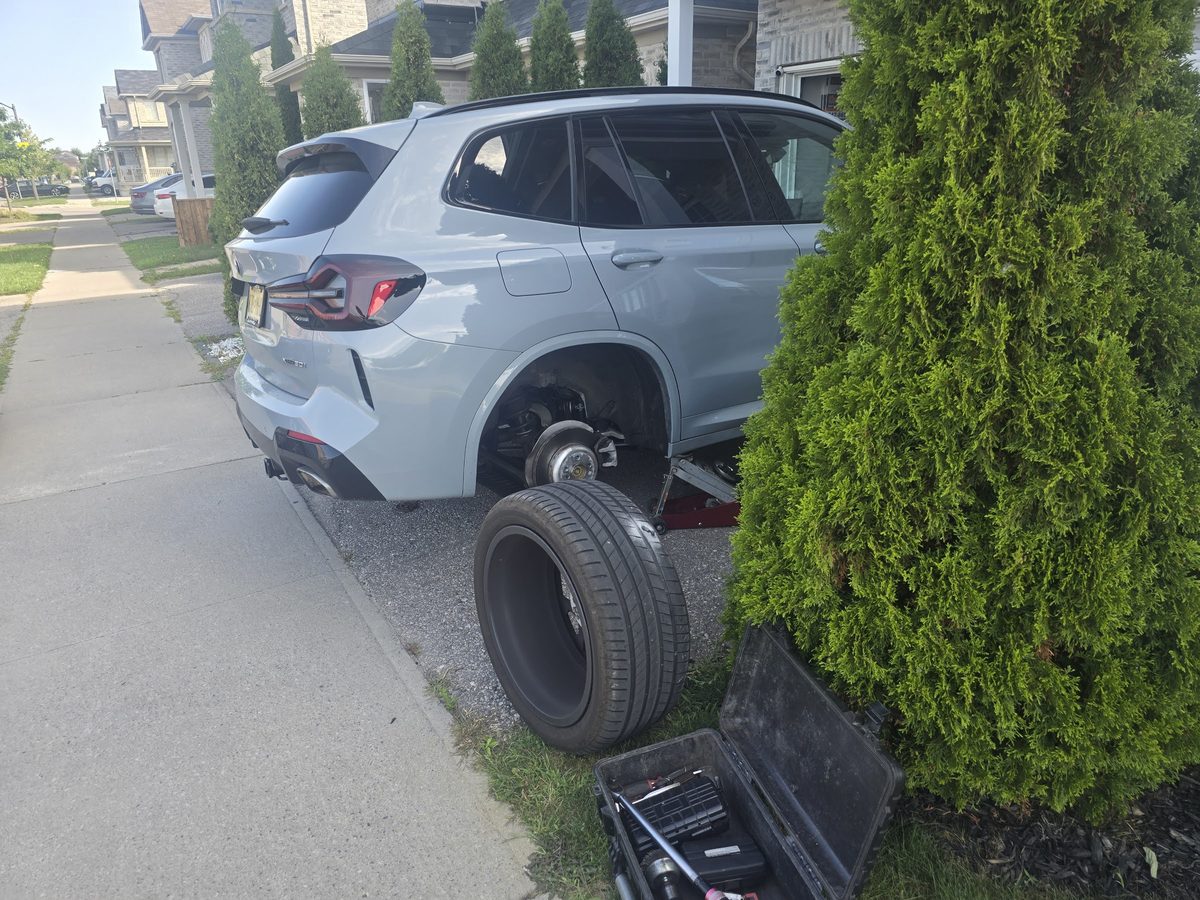Grey BMW iX with its rear wheel removed during a driveway tire service