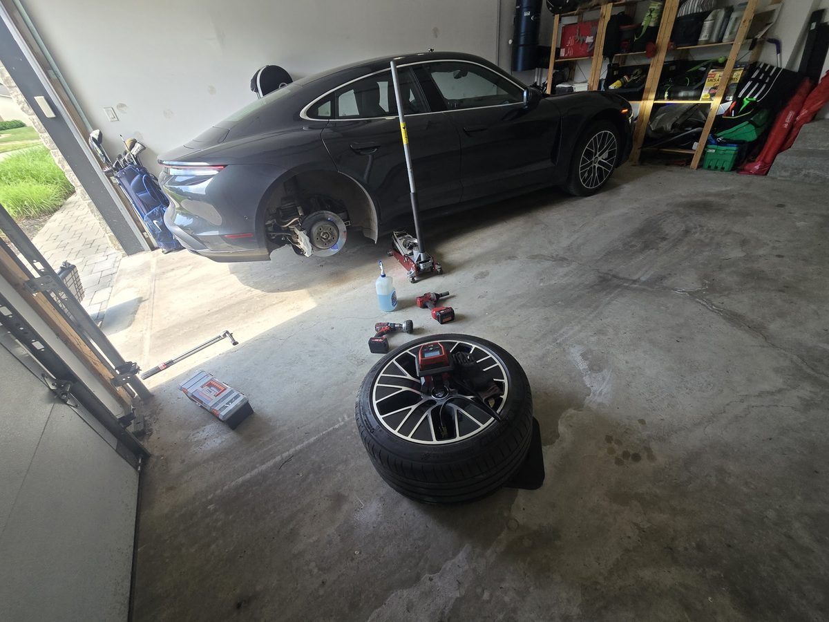 Silver Porsche Taycan with its rear wheel removed during a driveway tire service