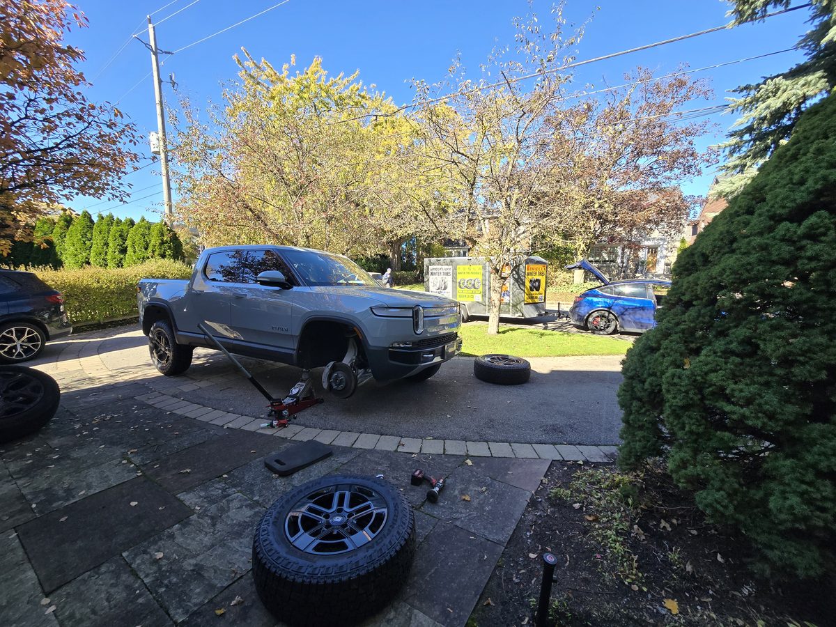 Grey-blue Rivian R1T with its front wheel removed during a winter driveway tire service